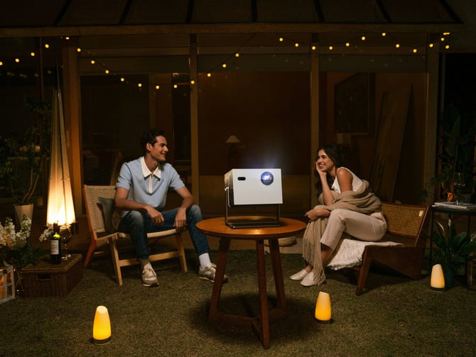 Couple watching a movie outdoors with a portable projector and string lights at night